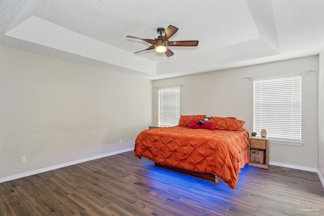 bedroom featuring dark wood-type flooring, multiple windows, a raised ceiling, and a textured ceiling