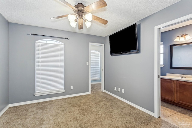 unfurnished bedroom featuring ceiling fan, light carpet, a textured ceiling, and ensuite bath