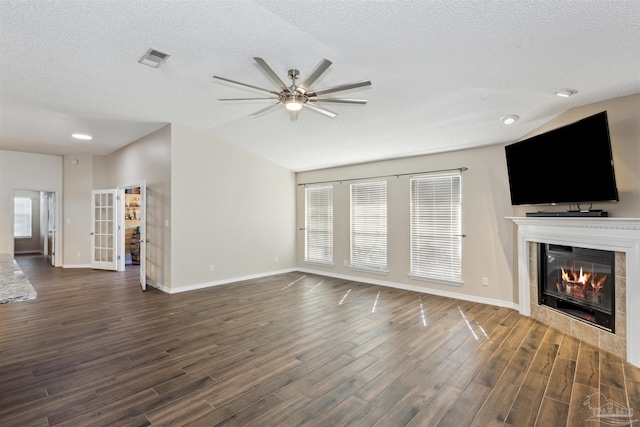 unfurnished living room featuring a tiled fireplace, dark wood-type flooring, lofted ceiling, and a textured ceiling