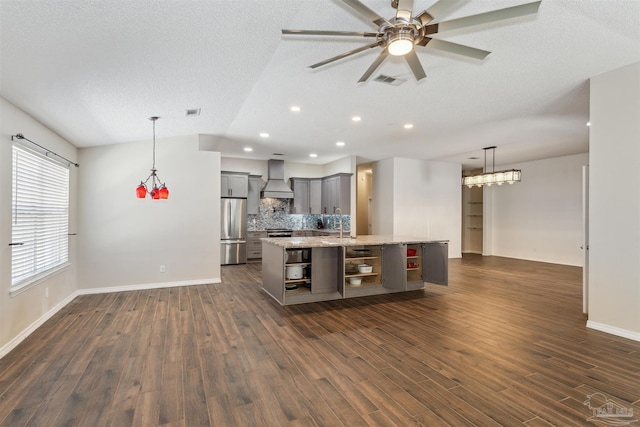 kitchen featuring premium range hood, light stone counters, stainless steel refrigerator, an island with sink, and pendant lighting