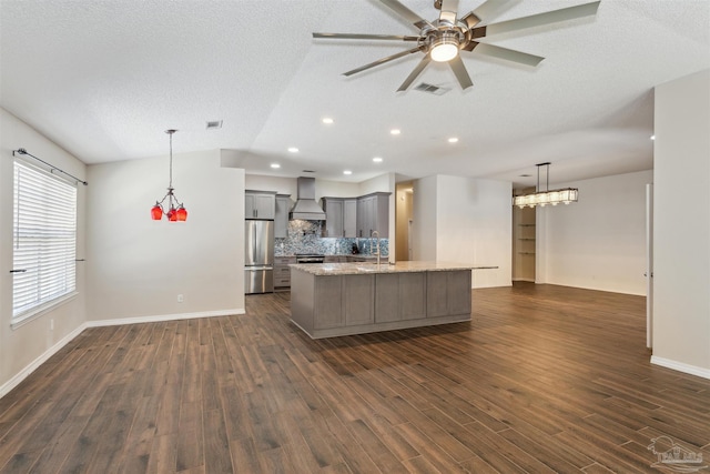 kitchen featuring custom exhaust hood, light stone counters, hanging light fixtures, a center island with sink, and appliances with stainless steel finishes