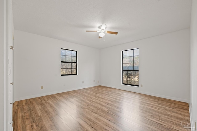 empty room featuring ceiling fan, light hardwood / wood-style floors, a textured ceiling, and a wealth of natural light