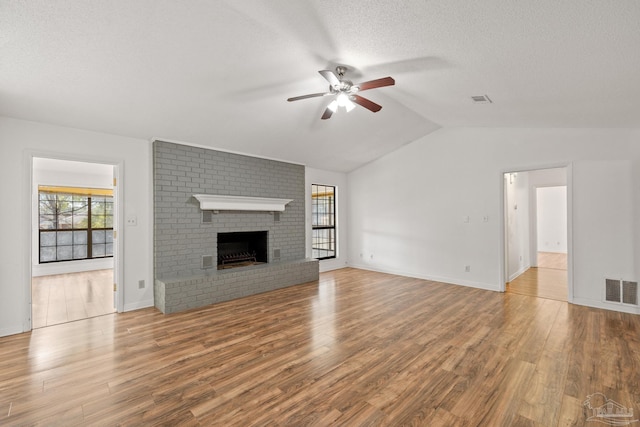 unfurnished living room featuring lofted ceiling, a fireplace, light hardwood / wood-style flooring, and a textured ceiling