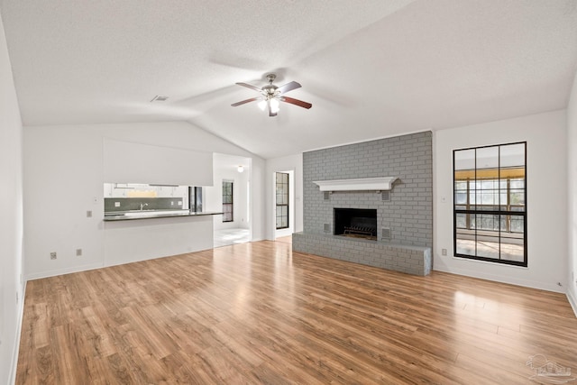 unfurnished living room featuring lofted ceiling, a fireplace, light hardwood / wood-style flooring, and ceiling fan