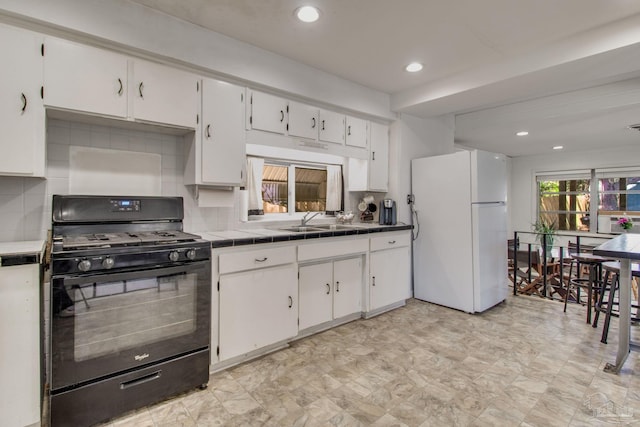 kitchen with black gas stove, a sink, freestanding refrigerator, and white cabinetry