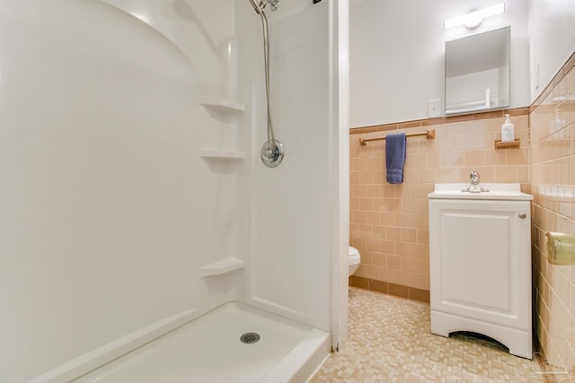 bathroom with toilet, a wainscoted wall, a shower stall, and tile walls