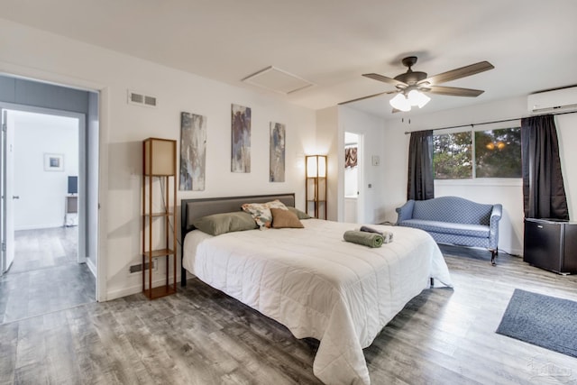 bedroom with attic access, baseboards, visible vents, wood finished floors, and a wall mounted AC