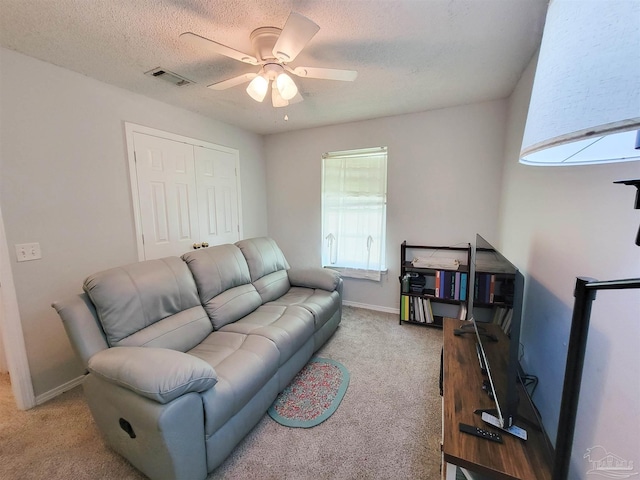 living area featuring light carpet, a ceiling fan, visible vents, and a textured ceiling