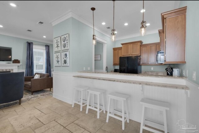 kitchen featuring a kitchen bar, black refrigerator, hanging light fixtures, and ornamental molding