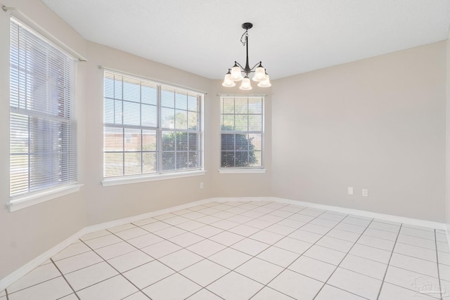 empty room featuring baseboards, light tile patterned floors, and a notable chandelier