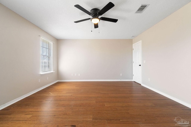 spare room with a textured ceiling, wood finished floors, visible vents, and baseboards