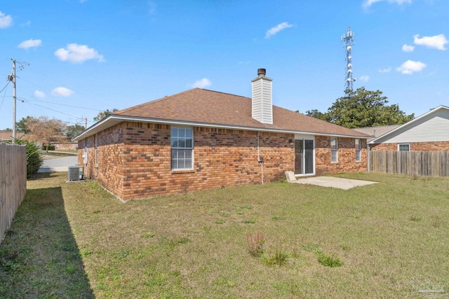 rear view of property featuring brick siding, a chimney, a lawn, central AC unit, and fence