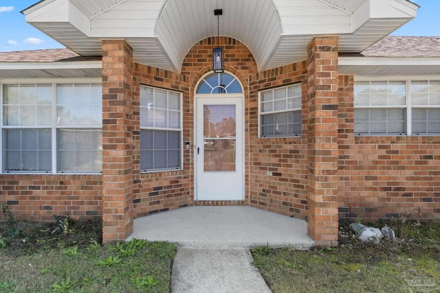 view of exterior entry featuring brick siding and roof with shingles