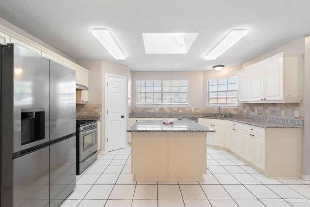 kitchen featuring light tile patterned floors, decorative backsplash, appliances with stainless steel finishes, a center island, and a sink