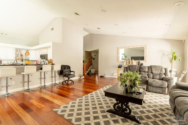 living room featuring hardwood / wood-style flooring, a textured ceiling, sink, and high vaulted ceiling