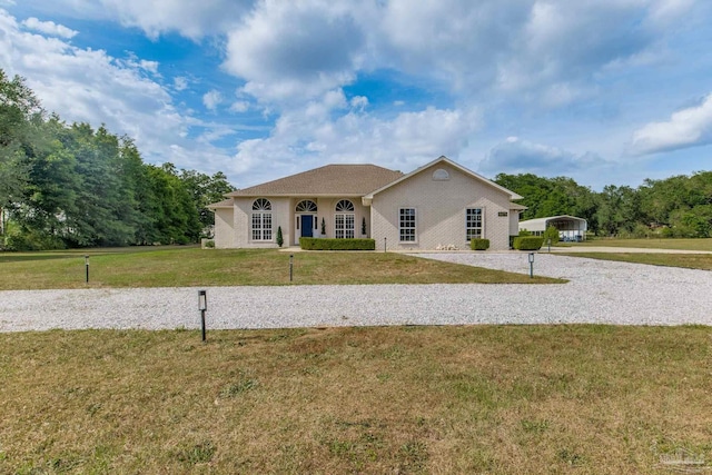 view of front facade with a front yard, a carport, and gravel driveway