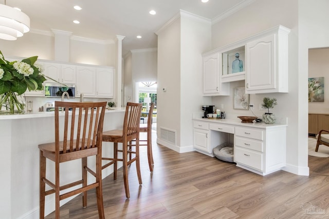 kitchen featuring stainless steel microwave, built in study area, light wood-type flooring, a breakfast bar area, and visible vents