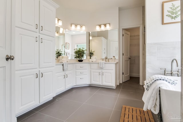 bathroom with double vanity, tile patterned floors, a freestanding tub, and a walk in closet