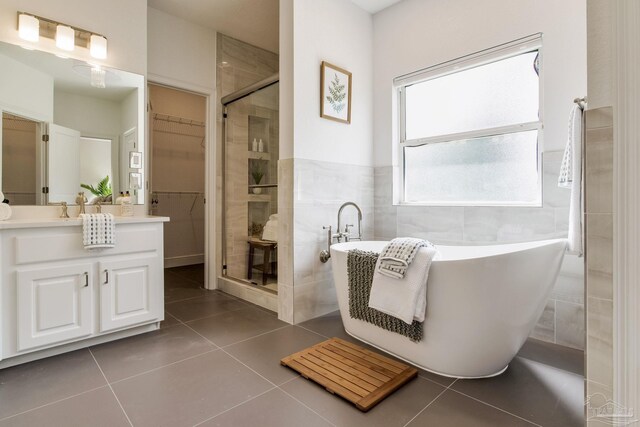 bathroom with a stall shower, tile patterned flooring, a freestanding tub, vanity, and a spacious closet