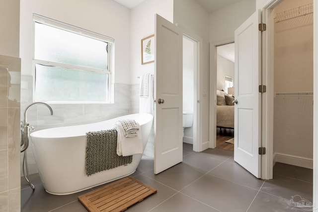 bathroom with a freestanding bath, tile walls, a wainscoted wall, and tile patterned flooring
