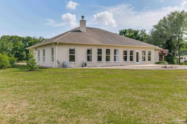 back of property with a yard, roof with shingles, brick siding, and a chimney