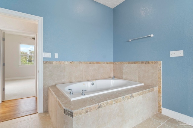 bathroom with hardwood / wood-style flooring, tiled tub, a textured ceiling, and ceiling fan