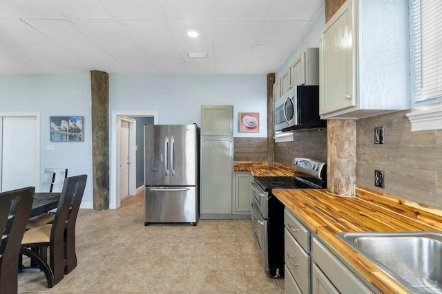 kitchen featuring gray cabinets, wooden counters, appliances with stainless steel finishes, light tile patterned floors, and backsplash