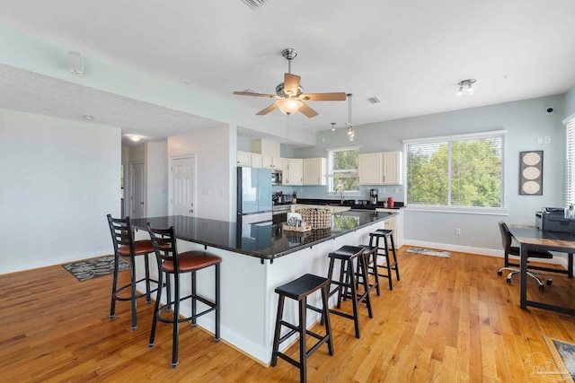 kitchen with a center island, appliances with stainless steel finishes, light wood-type flooring, and a breakfast bar