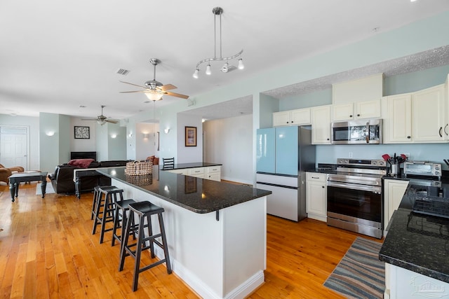 kitchen with ceiling fan, white cabinets, a breakfast bar area, light hardwood / wood-style floors, and appliances with stainless steel finishes