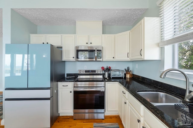 kitchen featuring dark stone counters, white cabinets, light hardwood / wood-style floors, appliances with stainless steel finishes, and sink