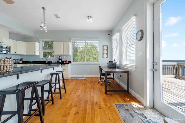 kitchen with decorative light fixtures, white cabinetry, light wood-type flooring, sink, and a breakfast bar