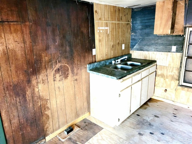 kitchen with dark countertops, wood walls, white cabinetry, and a sink