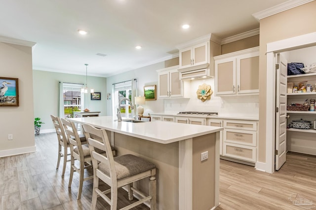 kitchen featuring hanging light fixtures, a breakfast bar area, tasteful backsplash, a kitchen island with sink, and light hardwood / wood-style flooring