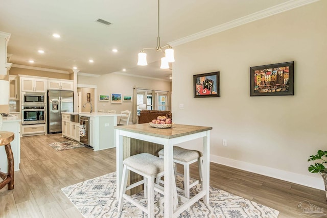 kitchen featuring appliances with stainless steel finishes, hanging light fixtures, an island with sink, white cabinets, and light hardwood / wood-style flooring