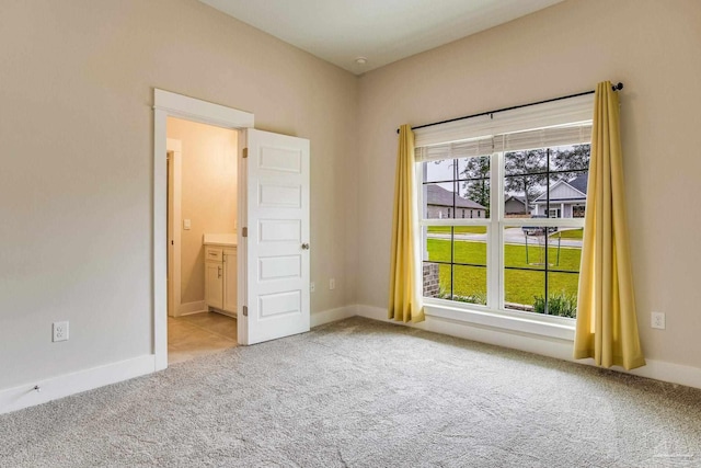 unfurnished bedroom with light colored carpet, multiple windows, and connected bathroom