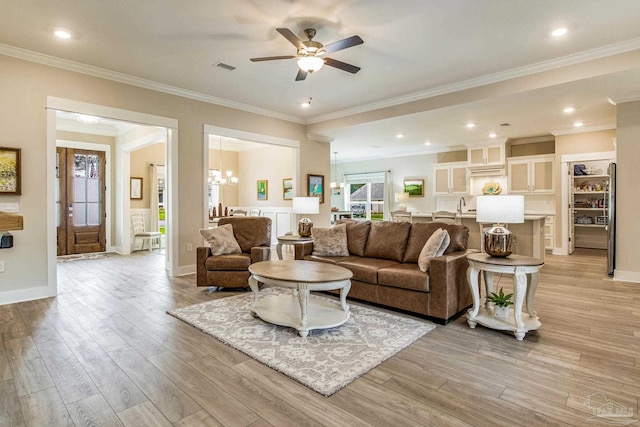 living room featuring ornamental molding, ceiling fan with notable chandelier, light hardwood / wood-style flooring, and sink