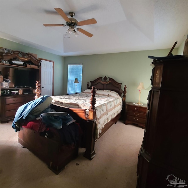 bedroom with light colored carpet, a raised ceiling, and ceiling fan