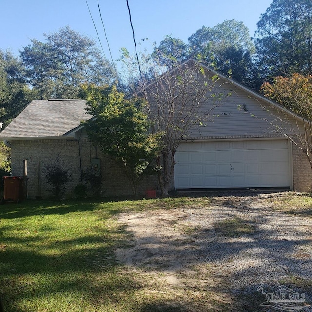 view of side of property with a lawn, gravel driveway, roof with shingles, a garage, and brick siding