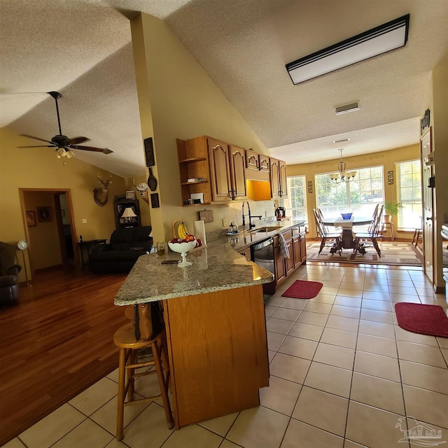 kitchen with vaulted ceiling, light tile patterned floors, dishwashing machine, brown cabinetry, and open shelves
