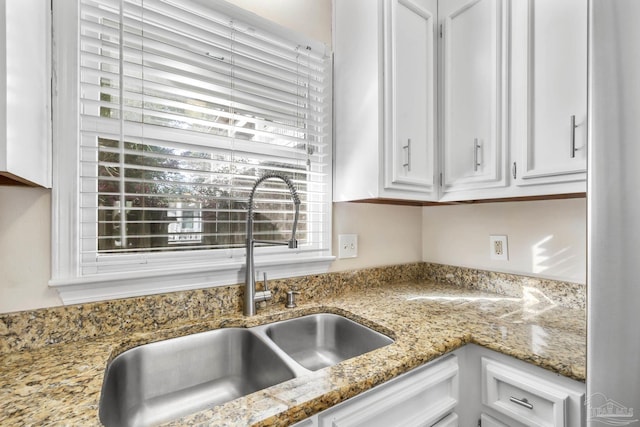 kitchen with plenty of natural light, white cabinetry, a sink, and light stone countertops