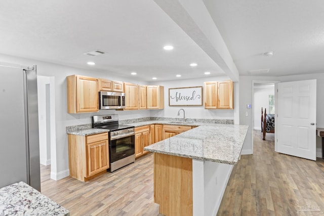 kitchen with appliances with stainless steel finishes, light brown cabinets, a sink, and light stone counters