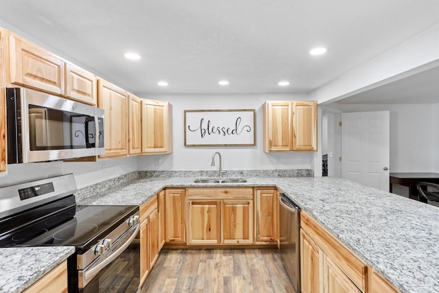 kitchen with light stone counters, light brown cabinets, a sink, appliances with stainless steel finishes, and light wood finished floors