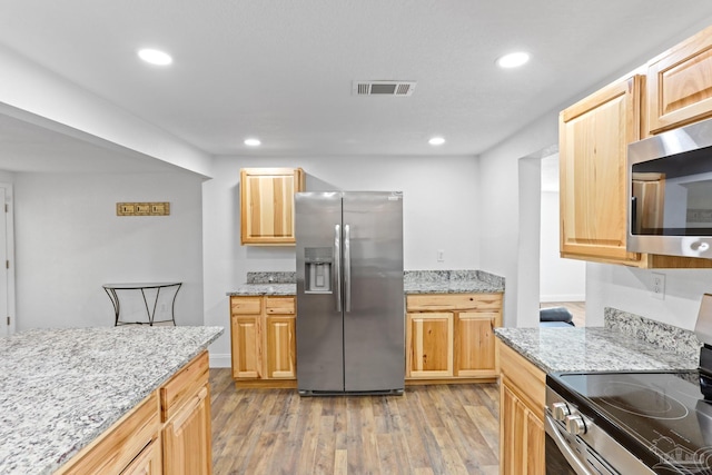 kitchen with light stone countertops, visible vents, appliances with stainless steel finishes, and light wood-style flooring