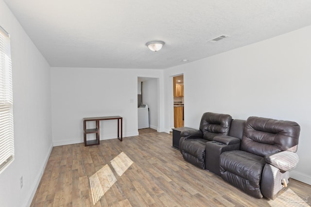 living area with visible vents, a textured ceiling, wood finished floors, washer / dryer, and baseboards