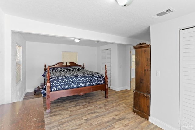 bedroom with visible vents, a textured ceiling, baseboards, and wood finished floors