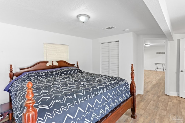 bedroom with a closet, wood finished floors, visible vents, and baseboards