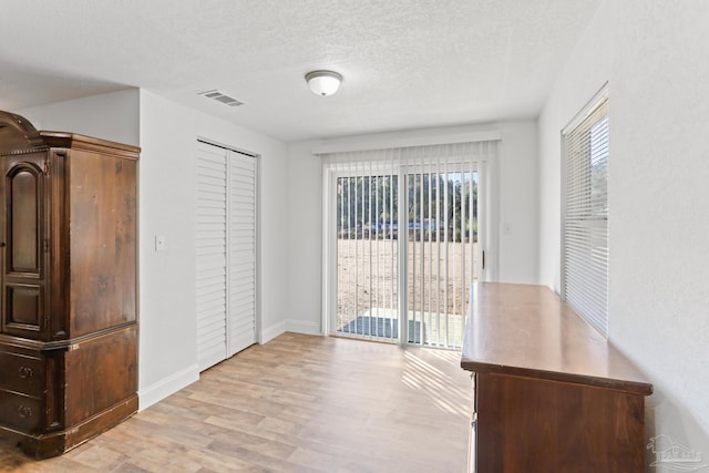 unfurnished bedroom with visible vents, access to outside, a textured ceiling, light wood-style floors, and a closet