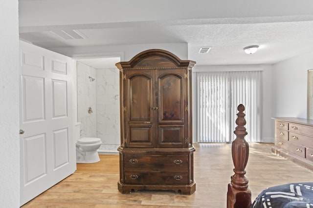 bedroom with visible vents, a textured ceiling, ensuite bath, and light wood-style flooring