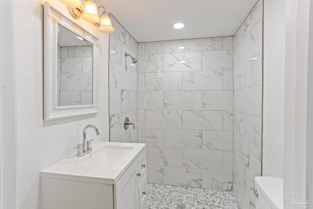 bathroom with a tile shower, vanity, and toilet