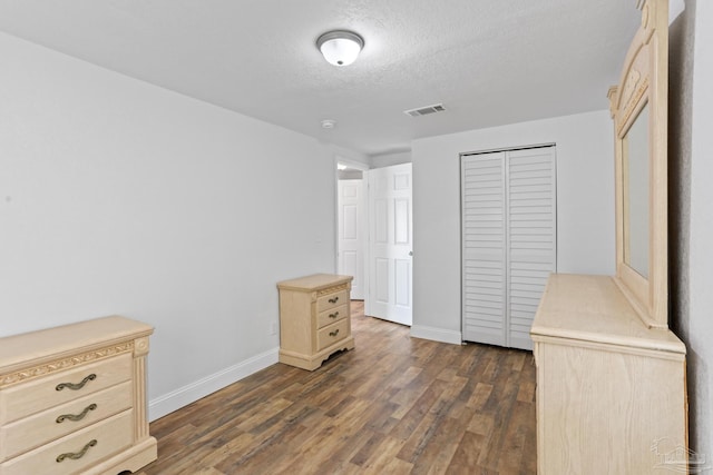 unfurnished bedroom with baseboards, visible vents, dark wood-style floors, a textured ceiling, and a closet